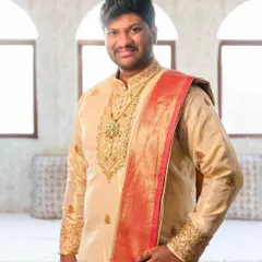 A closer look at a custom Kache Panche set. This groom's outfit features a beige silk kurta with intricate gold zardozi work on the neckline and cuffs, paired with a contrasting red and gold silk angavastram.
