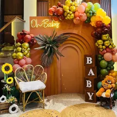 A warm and earthy baby shower theme with a terracotta-colored backdrop. The decor is enhanced with a colorful balloon garland, a peacock chair, "BABY" blocks, and sunflower accents.