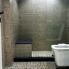 This bathroom features a glass partition for the shower area, which keeps the space feeling open. The textured wall tiles contrast nicely with the patterned floor.
