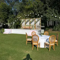 A wide view of the outdoor daytime stage. The white and gold structure, adorned with white roses, looks fresh and elegant on the green lawn.