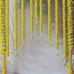 A simple yet beautiful Haldi backdrop. The design consists of a frame with hanging garlands of bright yellow marigolds against a clean white curtain.