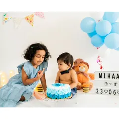 A big sister helps her baby brother with his first birthday cake. Sibling involvement makes milestone sessions even more special and memorable.