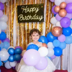 A happy birthday girl surrounded by a sea of colorful balloons. Her bright smile shows the pure joy of her special day.