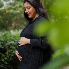 A serene solo portrait of the mom-to-be, gently holding her baby bump. The lush green background provides a calm and natural atmosphere for this maternity photo.