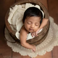 A two-month-old baby peeks over the edge of a rustic wooden bucket, showing that beautiful portraits are possible even after the first few weeks. That little smirk is everything.