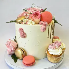 For a more sophisticated theme, I created this elegant floral cake. It's a smooth buttercream cake with a delicate gold drip, adorned with fresh pink roses, macarons, and paired with coordinating cupcakes for a complete, classy look.