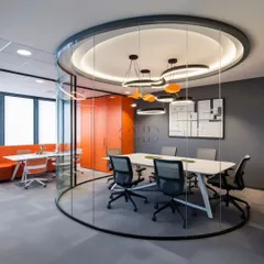 This curved glass meeting room offers acoustic privacy without sacrificing visual connection to the rest of the office. The design choice reflects a modern work culture of transparency and collaboration, complemented by unique pendant lighting that adds a sculptural element.