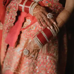 A close-up of the bride's hands, showcasing her beautiful red chooda bangles and intricate mehndi.