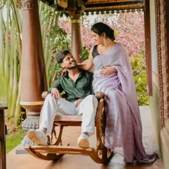 A couple sharing a tender moment on a rocking chair on the porch of a traditional house. The mother-to-be's lavender saree adds a soft, elegant touch.