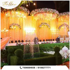 An opulent outdoor reception setup featuring a grand stage with cascading floral chandeliers and a manicured hedge fountain as a unique centerpiece. The warm lighting creates a luxurious and inviting atmosphere.
