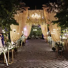 A grand entrance for a sangeet night, featuring a dramatic walkway with golden sequin drapes, crystal chandeliers, and a custom welcome sign for the couple.