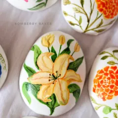 A close-up of a hand-painted Easter egg made from homemade cashew marzipan, featuring a beautiful yellow lily.