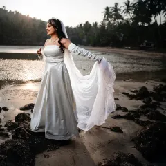 A stunning bridal portrait on a Goa beach at sunset. The golden light and the way she holds her flowing dress create a moment of pure grace and beauty.