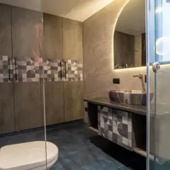 This contemporary bathroom showcases a unique patterned tile used on both the vanity and as an accent strip in the shower. The backlit arched mirror adds a soft, flattering glow to the space.
