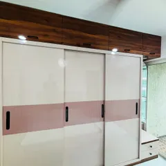 A wide, floor-to-ceiling sliding wardrobe in a two-tone design of beige and dusty rose. The wooden loft cabinets above provide additional storage for less frequently used items.