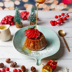 A beautiful Christmas pudding being drizzled with syrup, surrounded by festive decorations.