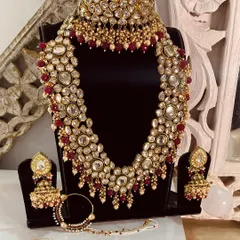 A complete Kundan bridal set in a traditional red and gold palette. This set includes a choker, a long necklace, jhumka earrings, a nath, and a maang tikka, ensuring you have every piece for your main wedding day.