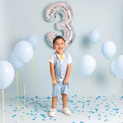 The pure joy of turning three! This little boy is having the time of his life celebrating with blue balloons and confetti.