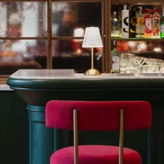 Detail is everything in creating ambiance. In this club bar, the contrast between the plush red velvet of the stool, the deep green paneling, and the warm glow from a classic table lamp creates a composition that feels both sophisticated and inviting.