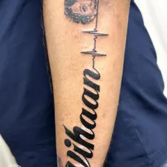 The final "Vihaan" name tattoo, shown on its own. The bold, clean script and the delicate heartbeat line create a beautiful and heartfelt piece that completely replaces what was there before.