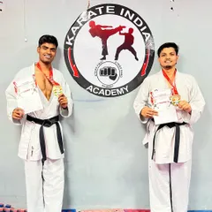 Champions at our dojo. Harshit and Jeetu back at the academy with their gold medals from the KIO National Championship, standing proudly in front of our logo.