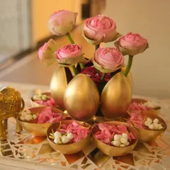 A close-up of the unique centerpiece. Pink lotus buds are arranged in golden vases, surrounded by small bowls of fresh petals and a golden elephant figurine for a touch of traditional charm.