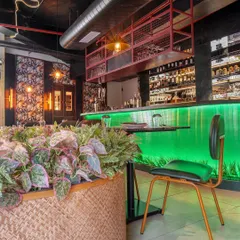 A large woven planter filled with lush greenery sits beside the glowing green bar at Burosu. We used natural elements to soften the industrial and neon features, creating a balanced and texturally rich environment.