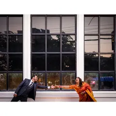 A playful, dynamic black and white shot of a couple reaching for each other. The architectural lines of the windows create a strong graphic element in the composition.