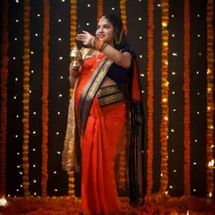 A festive and vibrant portrait celebrating tradition. The mother-to-be, dressed in a stunning orange saree, is surrounded by a curtain of marigolds and diyas, creating a truly magical atmosphere.