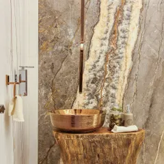 We brought nature indoors with this rustic-chic powder room. A hammered copper vessel sink sits atop a solid wood log pedestal, set against a backdrop of richly veined natural stone.