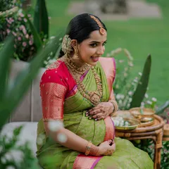 A serene moment from a Valaikappu photoshoot. The green and pink silk saree is draped to create a look of pure grace and maternal glow.