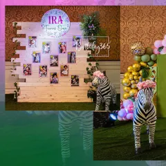 A fun and stylish jungle-themed birthday party for a little girl. The setup includes a rustic wooden pallet wall for displaying photos, life-sized zebra props wearing floral crowns, and a vibrant balloon garland.
