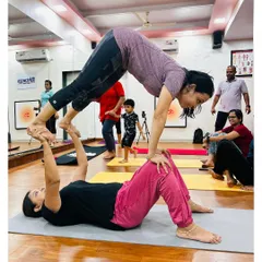 A student acts as the base while another balances in a downward dog variation. This Acro Yoga pose requires core strength and stability from both partners.