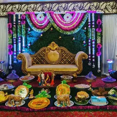A grand and traditional Seemantham ceremony stage. We designed this with a lush green and floral backdrop, an ornate golden sofa, and a full display of beautifully arranged ceremonial plates.