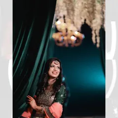 A beautiful portrait of the bride during her pre-wedding festivities. She is peeking from behind a green curtain, with a warm chandelier in the background, creating a lovely candid-style shot.