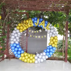 An outdoor birthday balloon ring in blue, yellow, and silver chrome. The setup includes foil letter balloons to spell out the name 'Kajal'.