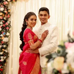 A classic engagement portrait. The groom's grooming is clean and sophisticated, matching the elegance of his white sherwani and complementing the bride's traditional saree.