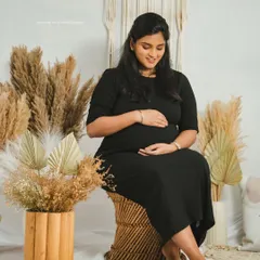A serene solo portrait of a mother-to-be seated in a boho-chic studio setting, gently cradling her baby bump.
