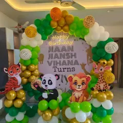 A jungle-themed birthday decoration for a home setting. This balloon arch features cute cutouts of a tiger, panda, lion, and giraffe, with a personalized "Happy Birthday" backdrop.