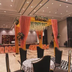 An elegant indoor mandap setup. The peach and gold fabric draping, combined with hanging floral arrangements, creates a sophisticated and traditional look.