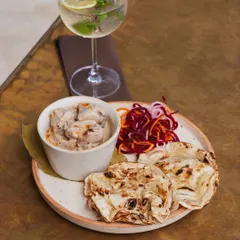 A plate of our creamy chicken malai with soft, layered naan and a side of pickled onions, paired with a refreshing gin and tonic. A simple, yet perfect, pairing.