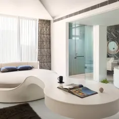 A bedroom designed for ultimate relaxation, featuring a custom, free-form circular bed that flows into an integrated side table. The adjoining bathroom, visible through a glass partition, includes a jacuzzi tub and a dramatic marble wall, creating a seamless, resort-like suite.