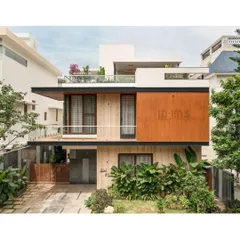 A frontal view of the same residence, showing the clean lines, cantilevered balcony, and rooftop terrace. The landscaping at the ground level softens the modern structure.