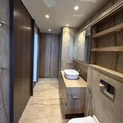 This bathroom is wrapped in the warm, earthy tones of natural stone tile. The clean lines of the wooden vanity and cabinetry create a seamless look, resulting in a space that feels both luxurious and grounded.