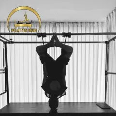 This is an artistic shot of an inversion on the Cadillac. It highlights the blend of strength, control, and flexibility that is at the heart of advanced Pilates work.