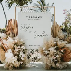 This welcome sign for a beach wedding features a modern design with pampas grass and dried palm leaves. The bohemian-chic aesthetic perfectly complements the natural, sandy surroundings.