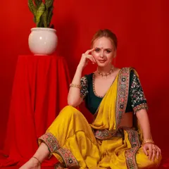 A full-length portrait of a model in a vibrant yellow and green saree, seated against a rich red background. This showcases a complete festive look, perfect for Diwali celebrations.