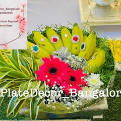 A bunch of fresh bananas decorated with kundan stones, arranged in a basket with bright red gerbera daisies and other foliage.