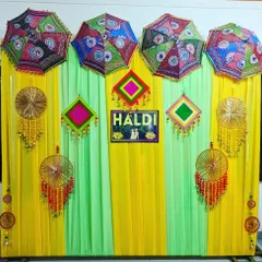 A colorful and festive Haldi backdrop. We used yellow and green drapes and decorated them with Rajasthani-style umbrellas, vibrant tassels, and a custom "HALDI" sign.