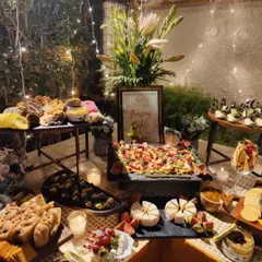 An evening view of a beautiful grazing table set up in a garden for a Diwali party. The fairy lights and candles add a magical touch to the spread of cheeses, breads, dips, and appetizers.
